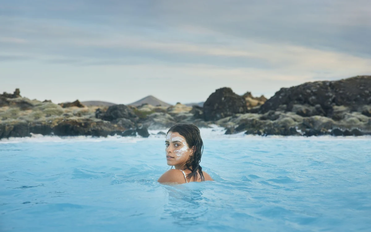 Bañistas en aguas geotermales azul pálido rodeados de roca de lava negra en Grindavik