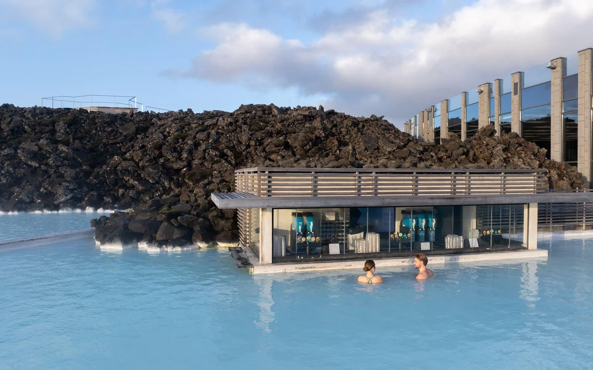 A low building beside milky Blue geothermal water enclosed by black lava