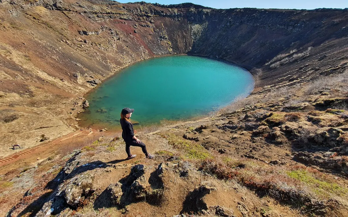 A person standing on the rim path above the coloured lake in the Kerid crater