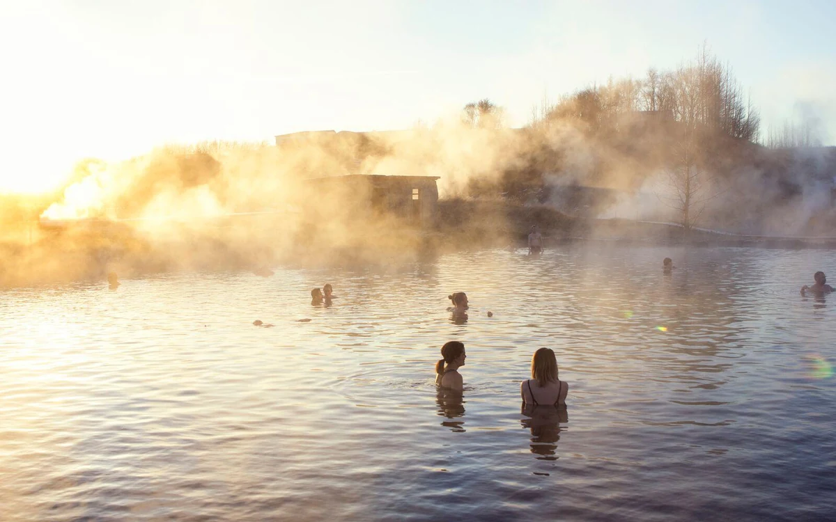 Bathers standing in a steaming outdoor pool in low Golden light