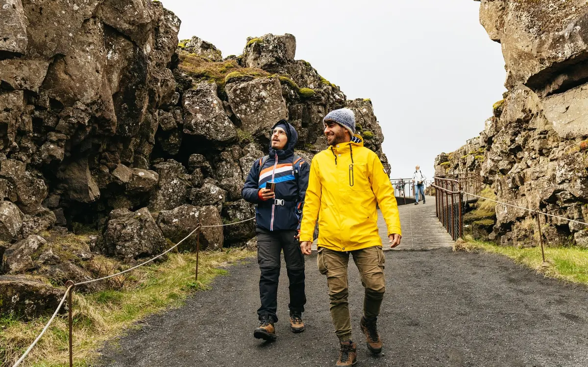 Two walkers on a gravel path between high rock walls at Thingvellir